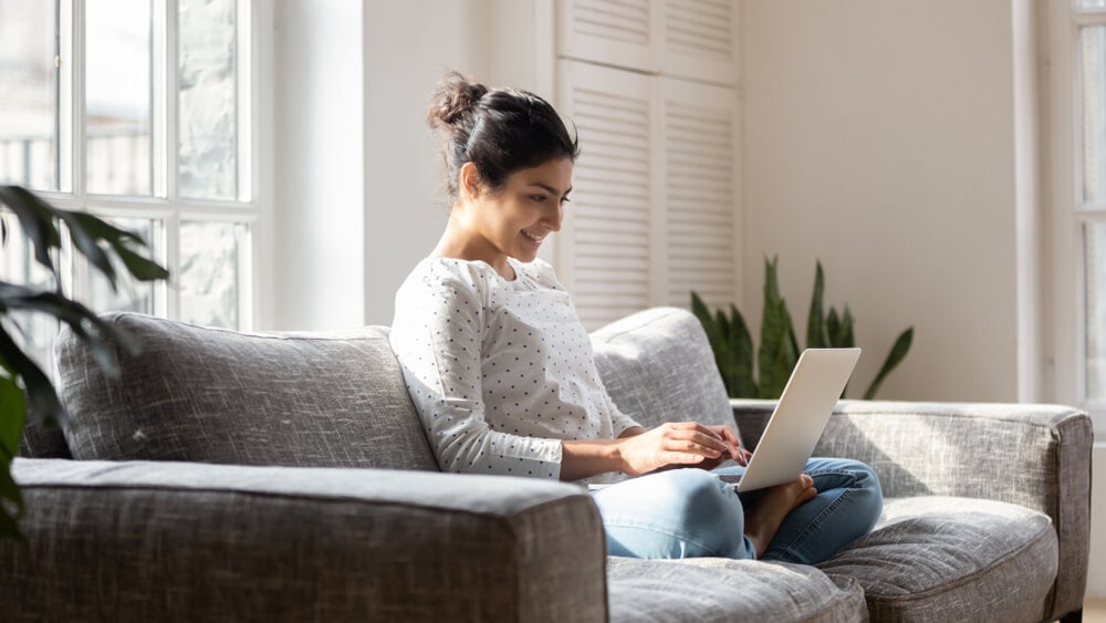 smiling woman in couch looking to save on car insurance in laptop