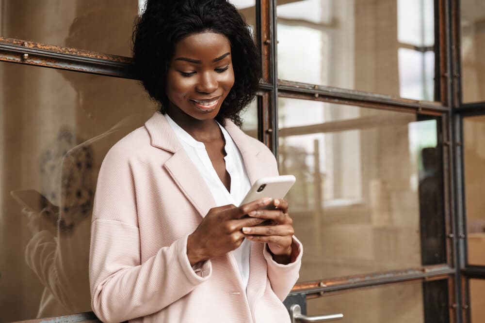 smiling young african american woman looking at smartphone