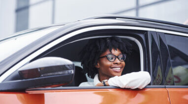 smiling young african american woman in drivers seat of car looking out the window