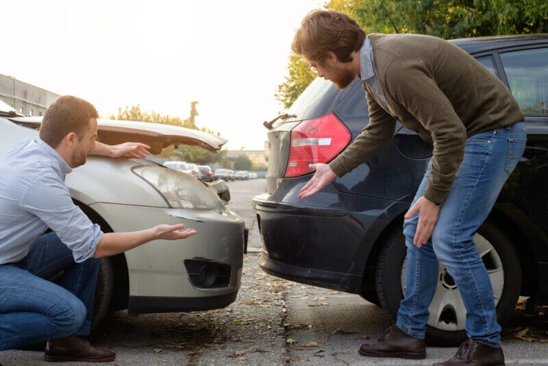 two men looking at vehicle collision damage after an accident