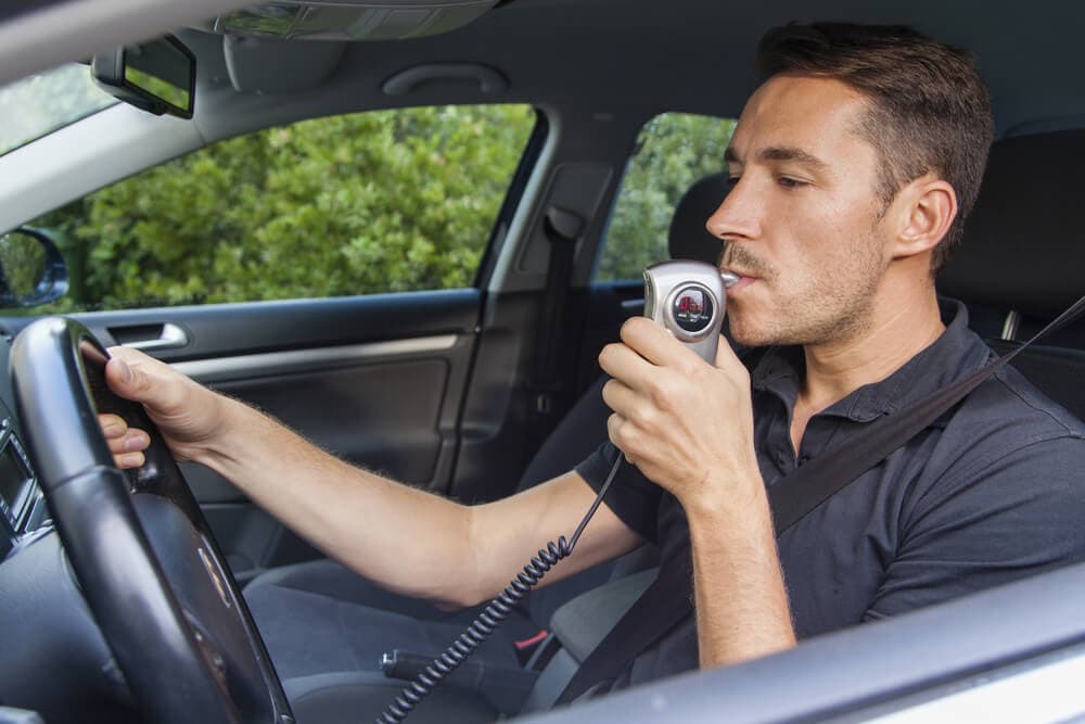 man behind wheel blowing into breathalyzer