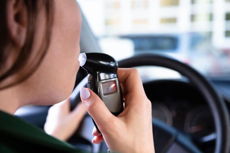 woman blowing into breathalyzer behind the wheel