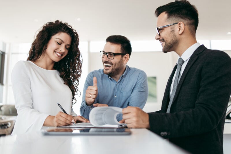 Young couple signing happily on the dotted line for car insurance