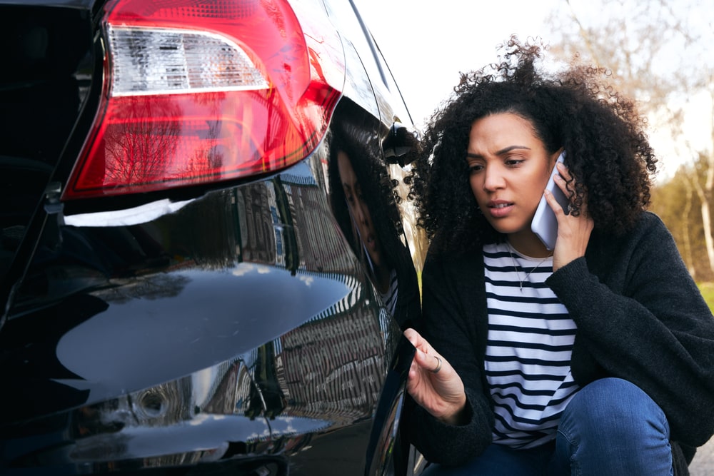 woman on phone looking at hit and run on car