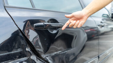 person pointing at hit and run dent on car