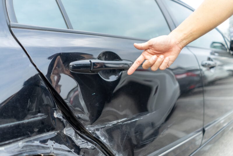 person pointing at hit and run dent on car