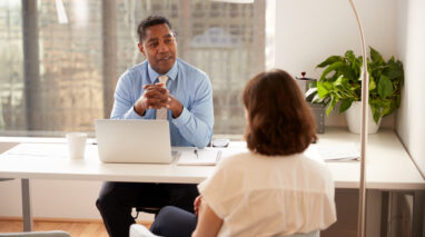 African American businessman behind desk and client in front with her back to camera