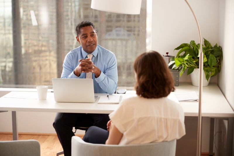 African American businessman behind desk and client in front with her back to camera