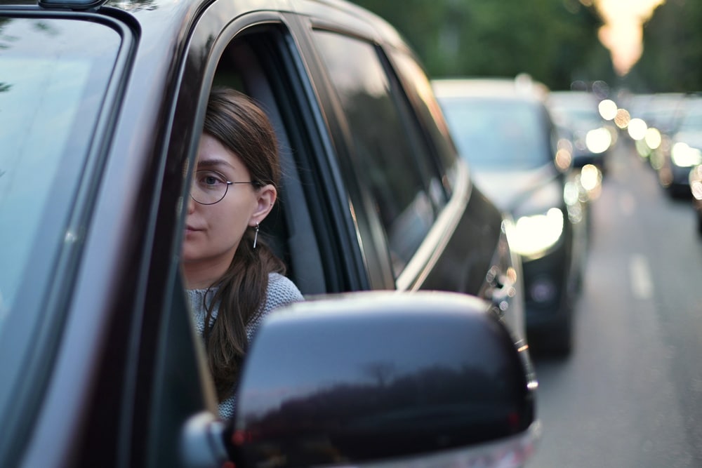 A young woman sits behind the wheel of her car in rush hour