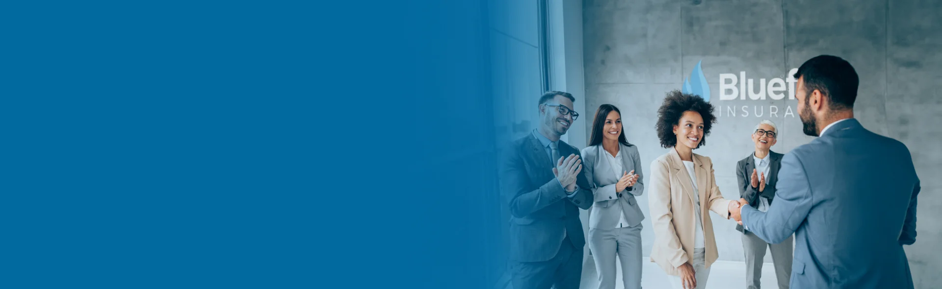 Diverse group of smiling business people clapping and standing in front of Bluefire wall.