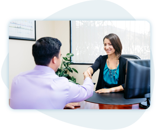 Businesswoman behind desk shaking hands with clients in front of window.